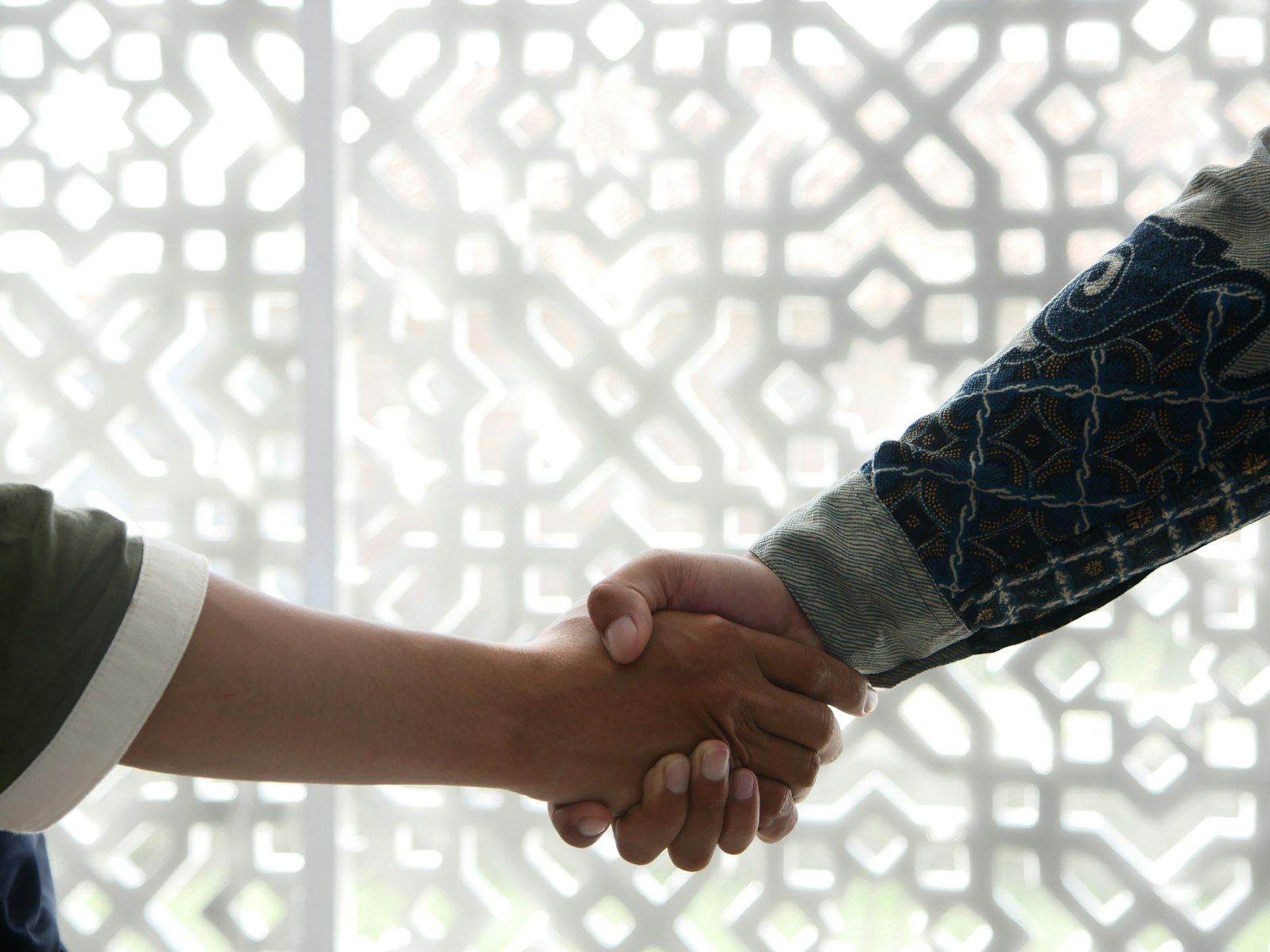 Two people shaking hands in front of a geometric screen